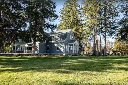 A large blue house surrounded by tall trees and a green lawn on a sunny day.