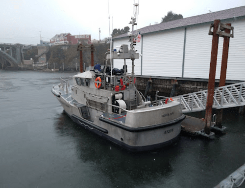 A gray boat docked at a pier on a foggy day, with buildings and a bridge in the background.