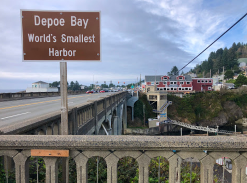 Sign for Depoe Bay, "World's Smallest Harbor," with a view of the harbor and surrounding buildings.