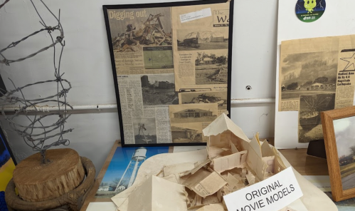 A display featuring a framed newspaper article and original movie models on a table with various artifacts.