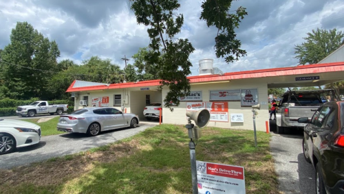 A drive-thru restaurant with a red roof, surrounded by cars and trees, under a cloudy sky.