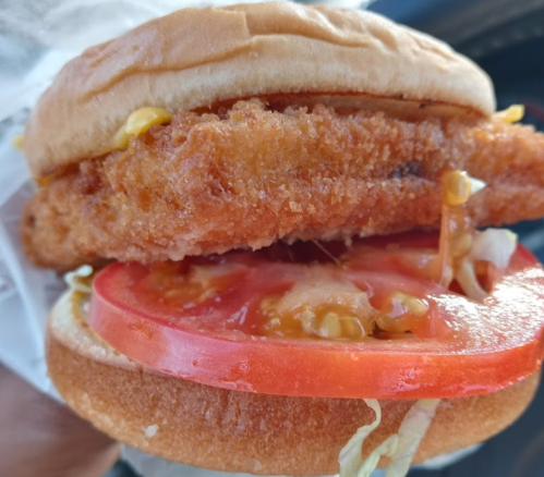 Close-up of a sandwich with a crispy chicken fillet, fresh tomato slices, lettuce, and mustard on a soft bun.