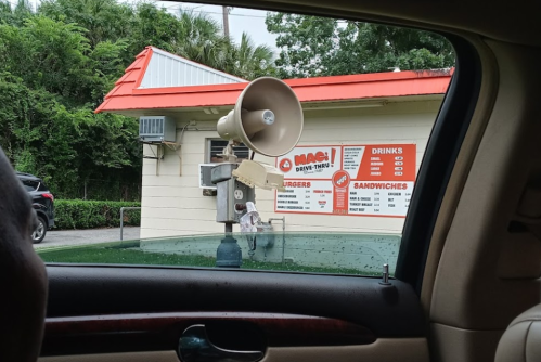 A drive-thru menu board with a speaker, displaying food and drink options, seen from a car window.