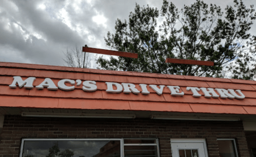 Sign for "Mac's Drive Thru" on a building with a cloudy sky in the background.