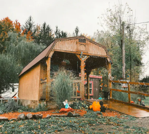 A cozy wooden cabin surrounded by autumn foliage and pumpkins, with a small figure sitting nearby.