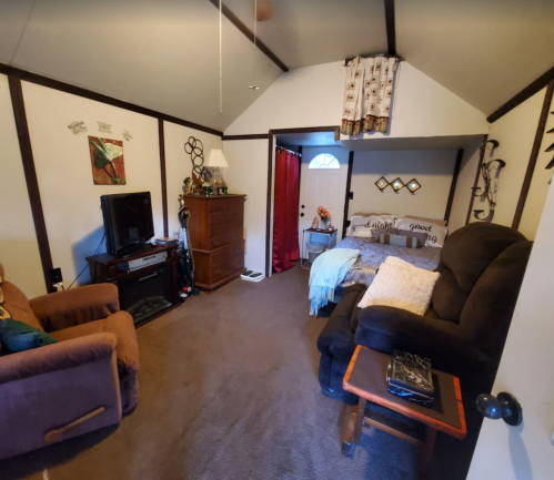 Cozy room with a bed, armchair, TV, and decorative elements, featuring a sloped ceiling and warm lighting.