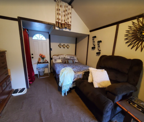 Cozy bedroom with a bed, armchair, and decorative wall accents, featuring a door and window for natural light.