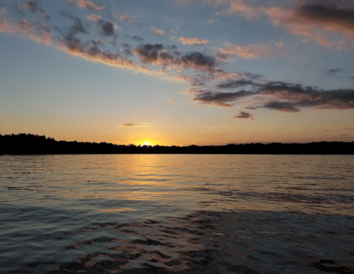 A serene sunset over a calm lake, with colorful clouds reflecting on the water's surface.
