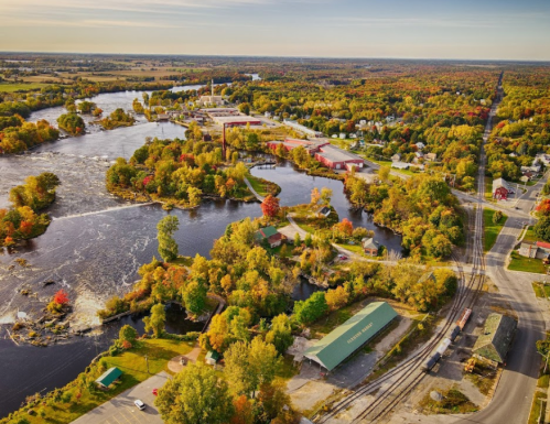 Aerial view of a vibrant autumn landscape with a river, industrial area, and colorful trees.