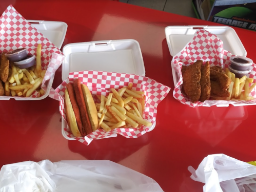 Three takeout containers with fries, chicken tenders, and hot dogs on a red table.