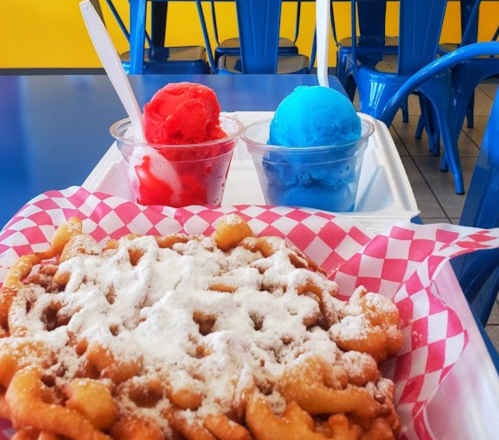 A plate of funnel cake dusted with powdered sugar, accompanied by two cups of red and blue sorbet.