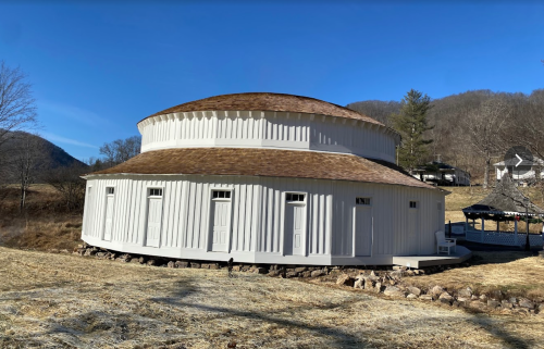 A round, white building with a circular roof, set in a rural landscape with mountains in the background.