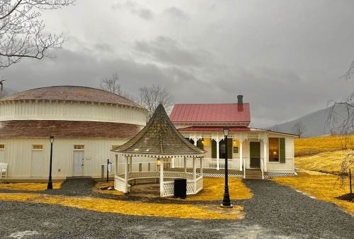 A quaint building with a circular structure and a gazebo, set against a cloudy sky and golden grass.