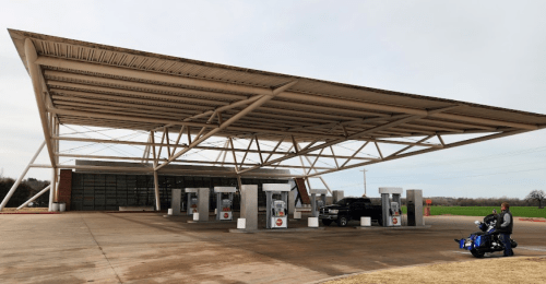Modern gas station with a large canopy, featuring multiple fuel pumps and a motorcycle parked nearby.