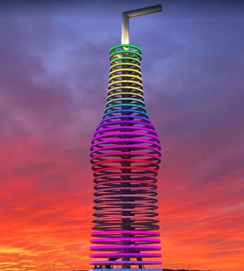 A colorful, spiraled tower resembling a bottle with a straw, set against a vibrant sunset sky.