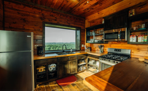 Cozy wooden kitchen with modern appliances, large window showcasing a scenic view of green hills.