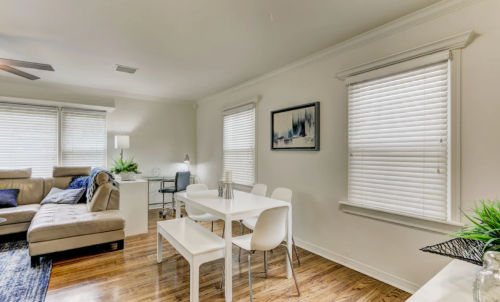 Cozy living space featuring a sofa, dining table, and desk with natural light from window blinds.
