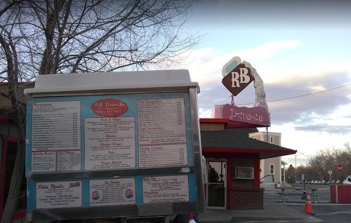 A drive-in restaurant with a menu board and a sign featuring "RB Drive-In" against a cloudy sky.