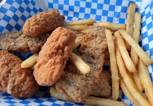 A basket of golden-brown fried chicken strips and French fries on a blue and white checkered paper.