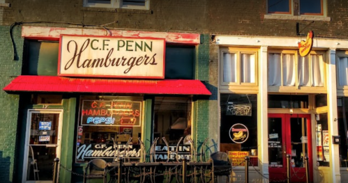 A vintage storefront with a sign reading "C.F. Penn Hamburgers" and a red awning, featuring outdoor seating.