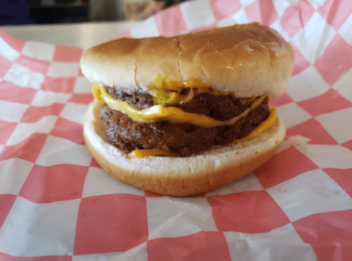 A close-up of a cheeseburger with two beef patties and melted cheese, served in a bun on a checkered paper.