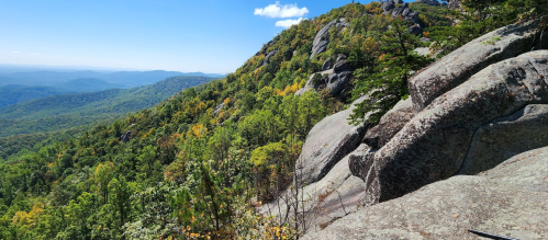 A panoramic view of a lush green mountain landscape with rocky outcrops under a clear blue sky.
