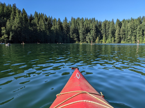 A red kayak on calm water, surrounded by lush green trees and a clear blue sky.