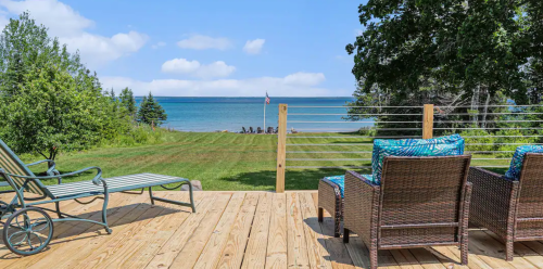 A serene lakeside view from a wooden deck with lounge chairs and a flag in the distance.