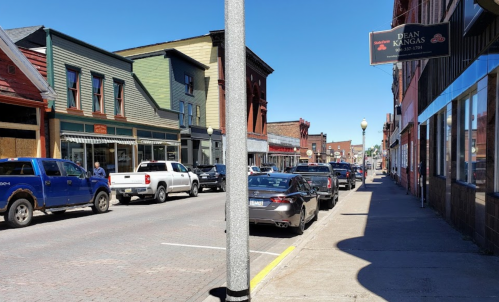 A street view of a small town with parked cars, colorful buildings, and clear blue skies.