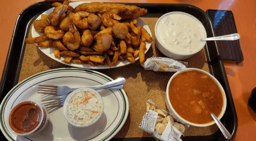 A tray with fried shrimp, fish, fries, coleslaw, soup, and two small packets of crackers.
