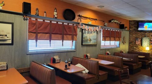 Cozy restaurant interior with brown booths, nautical decor, and large windows adorned with curtains and bunting.