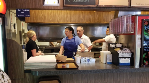 A busy restaurant kitchen with staff preparing food and interacting at the counter.