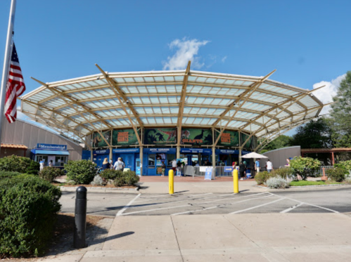 A modern building with a large glass roof, surrounded by greenery and a flagpole, under a clear blue sky.