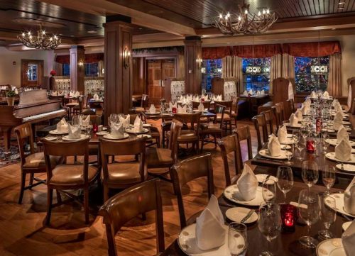 Elegant restaurant interior with neatly set tables, a piano, and warm lighting, creating a cozy dining atmosphere.