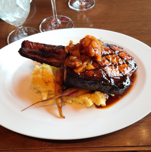 A grilled pork chop topped with a sweet glaze, served on a bed of creamy mashed potatoes with colorful vegetables.