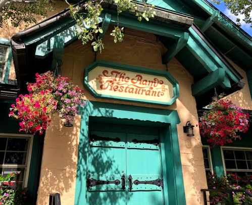A charming restaurant entrance with a sign reading "The Ram Restaurant" and colorful flower baskets hanging.