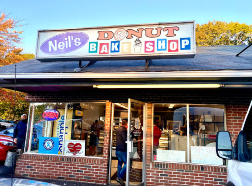A storefront of Neil's Donut & Bake Shop with a sign and people outside, showcasing a welcoming atmosphere.