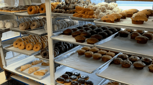 A display case filled with various baked goods, including donuts, muffins, and pastries on multiple trays.