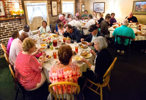 A large group of people enjoying a meal together at a round table in a cozy restaurant setting.