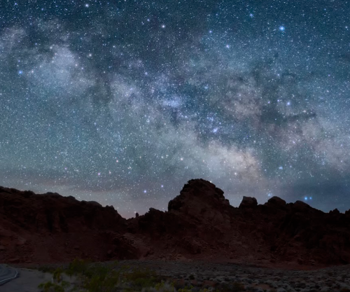A starry night sky filled with the Milky Way over rugged, dark rock formations.