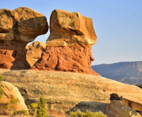 Two large, weathered rock formations stand side by side against a clear blue sky, with layered textures and colors.
