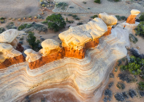 Aerial view of colorful rock formations and a winding path in a desert landscape, with a small figure walking.