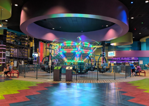 Colorful indoor amusement area featuring a small ride surrounded by seating and vibrant flooring.