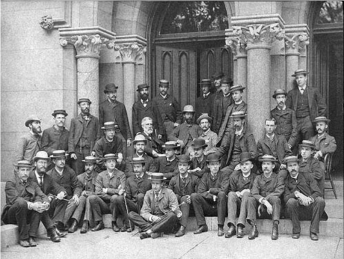 A large group of men in formal attire and hats, posed together on steps of a historic building.