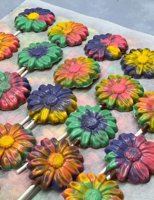 Colorful flower-shaped lollipops arranged on parchment paper, featuring vibrant swirls of pink, yellow, green, and blue.