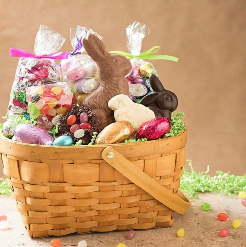 A woven basket filled with colorful Easter candies, chocolate bunnies, and decorative bags of treats.