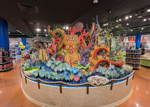 Colorful coral reef display made of candy, surrounded by shelves of merchandise in a vibrant store setting.