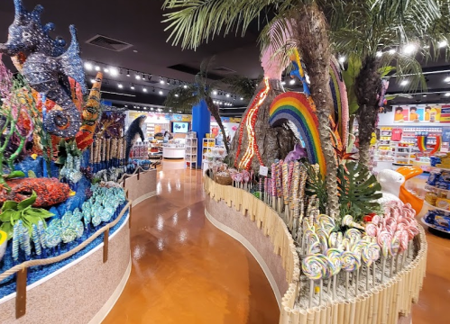 Colorful candy display with large decorative elements like palm trees and a rainbow, set in a vibrant store interior.