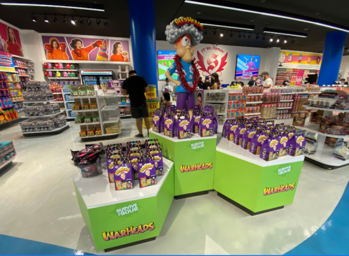 A colorful candy store display featuring Warheads products and a large character figure in a vibrant setting.