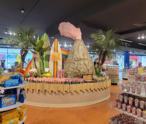 Colorful candy display featuring a volcano, rainbow, and palm trees in a vibrant store setting.